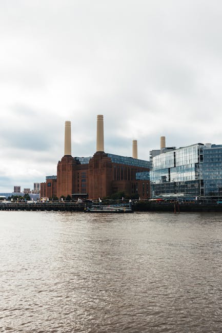 A low-angle view of Battersea Power Station's brick facade, showing its large, detailed brickwork with rectangular windows and a prominent white chimney extending into the cloudy sky. The building's m