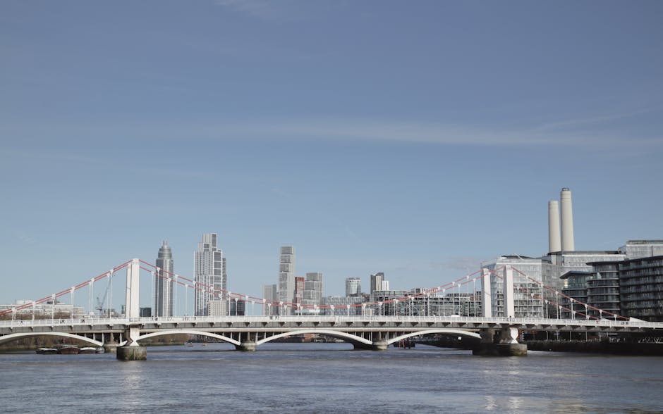 A wide view of Nine Elms in London featuring the Thames River in the foreground, a modern bridge crossing over the water with a series of tall contemporary buildings in the background, including high-